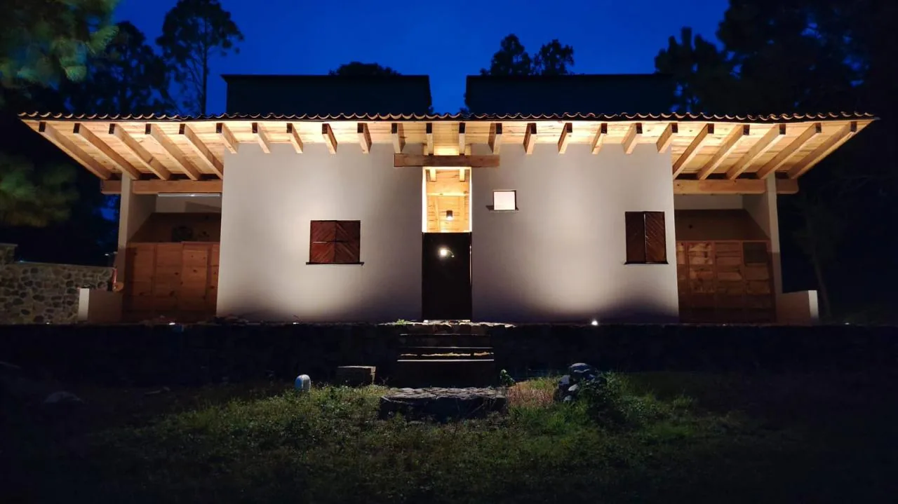 Fachada iluminada de una casa de Tlalli Residencial, con techo de vigas de madera y teja